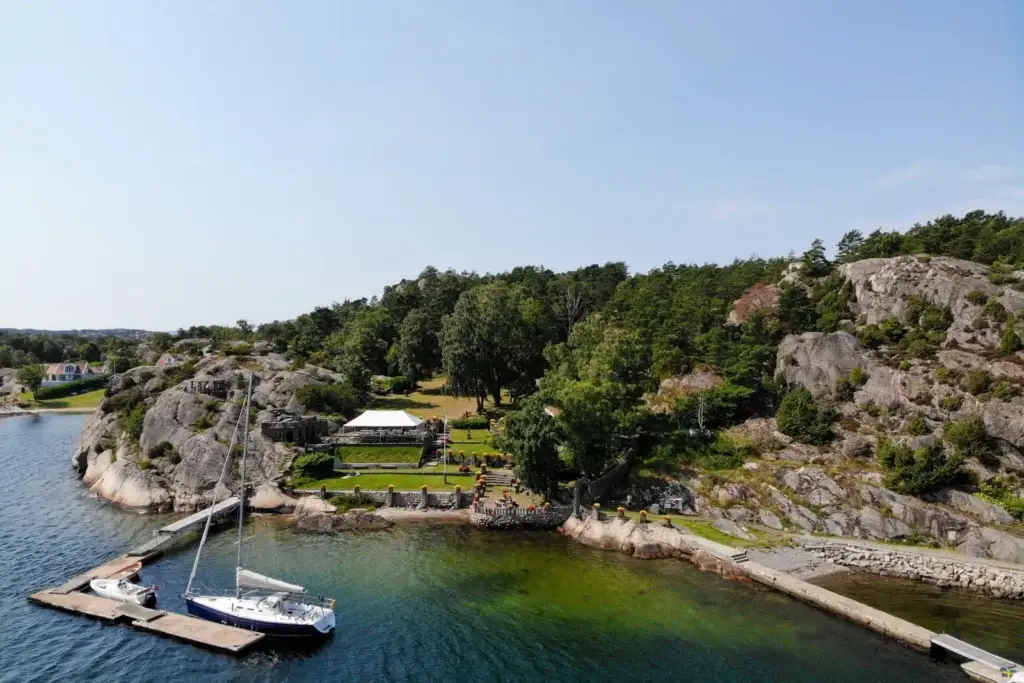 Alaskaträdgården med översiktlig by över stenträdgården med blommor och stora gräsytor och skog intill vatten gränsen och småbåtshamnen på Nord-långö.