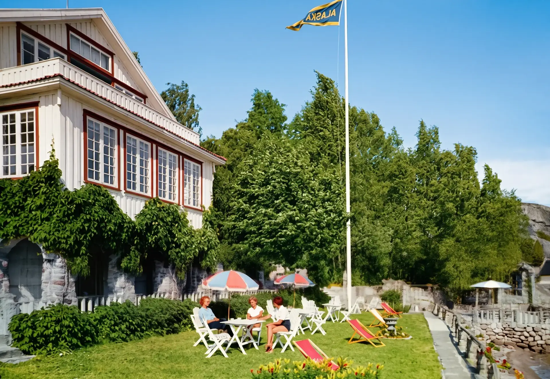 Alaskatradgardens-vardshus-och-grasmatta-intill-vattnet.webp